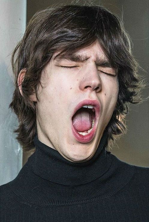 This may contain: a young man with his mouth open and tongue out in front of him, wearing a black turtle neck sweater