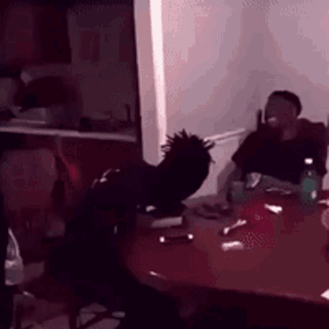a man is sitting at a table in a dark room with a bottle of water .