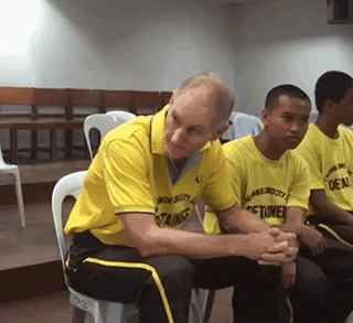 a man wearing a yellow shirt that says ' under security ' on it sits in a chair