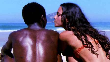 This may contain: a man and woman sitting on the beach looking at each other's back,