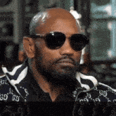 a bald man with a beard and sunglasses is wearing a gucci jacket .