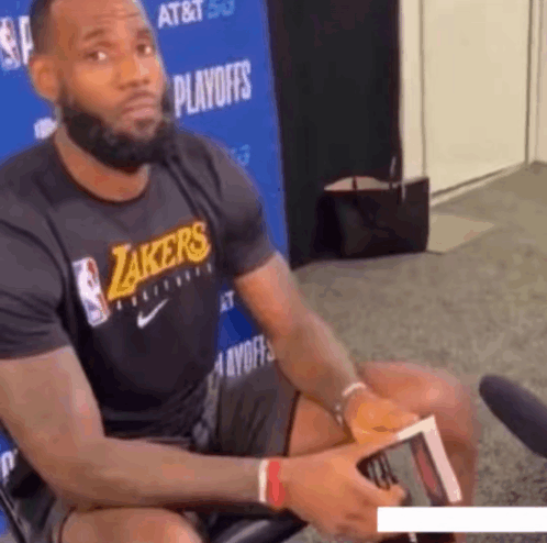 a man wearing a lakers t-shirt sits in front of a microphone