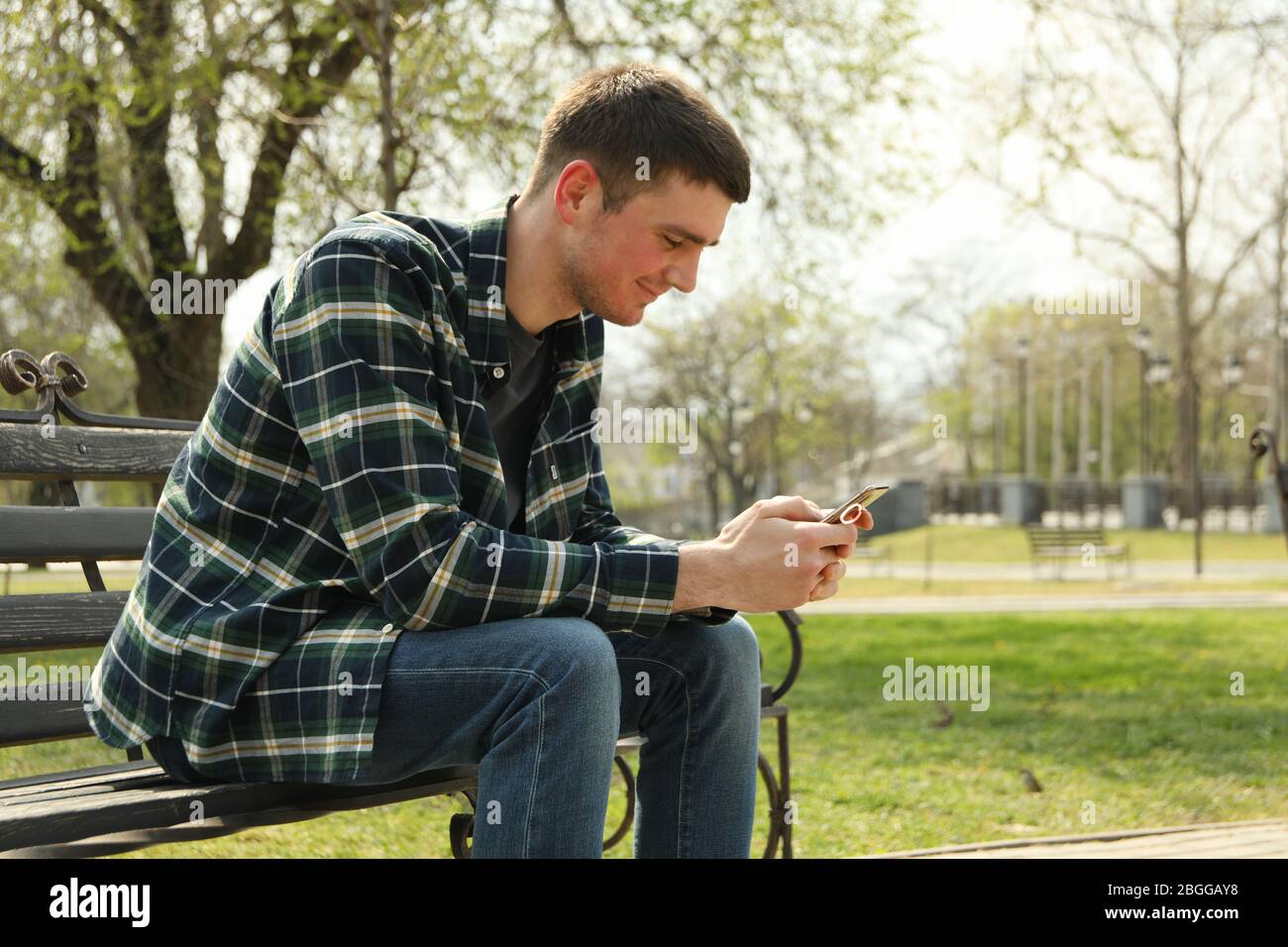 man-uses-smartphone-sitting-on-bench-in-park-2BGGAY8.jpg