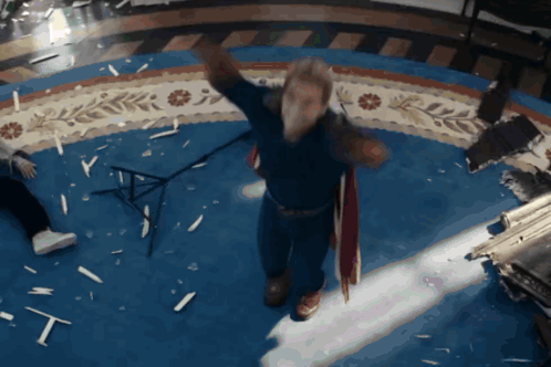 a man in a blue shirt is standing in a room with broken glass