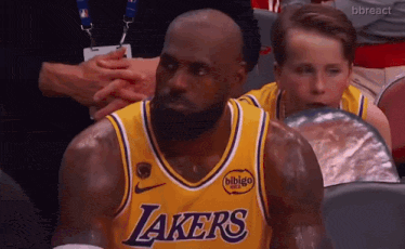 a man in a lakers jersey sits in a stadium