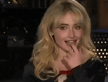 a close up of a woman with blonde hair covering her mouth with her hand .