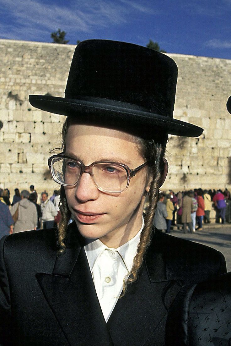 This may contain: a man with braids wearing a top hat and glasses in front of an old stone wall