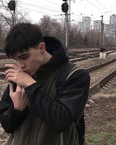 a young man standing in front of train tracks holding his hands to his face while looking at the camera