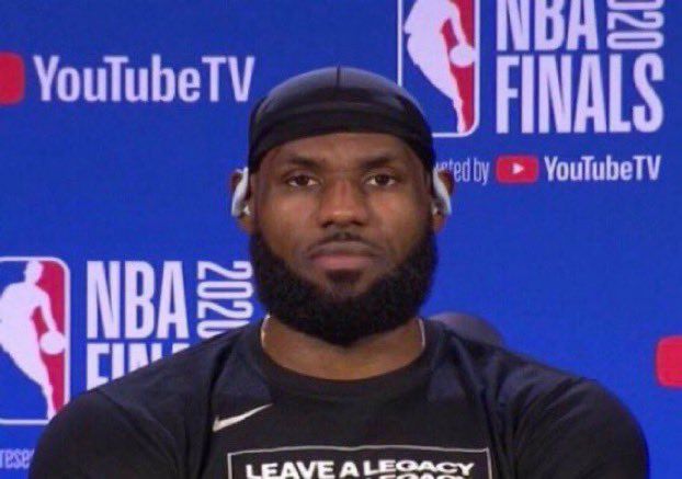 This may contain: a man with a beard wearing a black shirt and beanie sitting in front of a blue wall