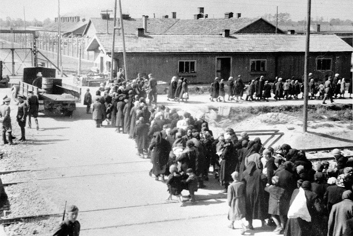 1200px-Birkenau_a_group_of_Jews_walking_towards_the_gas_chambers_and_crematoria.jpg