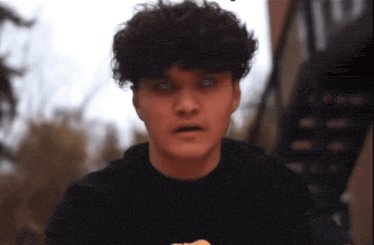 a young man with curly hair is wearing a black sweatshirt