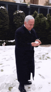 a man in a coat is standing in the snow holding a snowball
