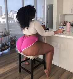 This may contain: a woman sitting on a stool drinking from a bottle in front of a kitchen counter