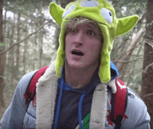a man wearing a green alien hat looks surprised in the woods