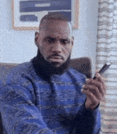 a man with a beard is sitting in a chair holding a cell phone .