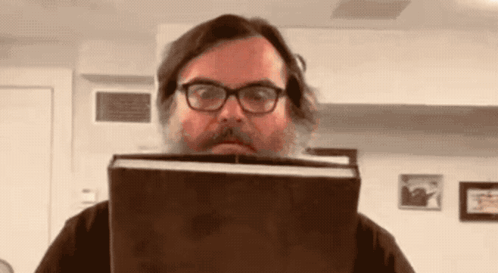a man with a beard and glasses is holding a book in front of his face