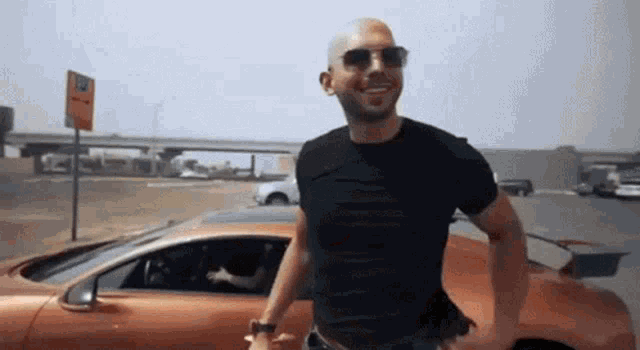 a man wearing sunglasses and a black shirt is standing in front of a car .