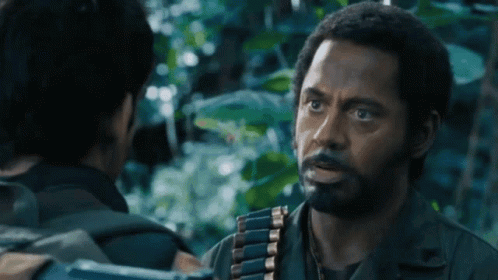 a man with a beard is talking to another man with a gun