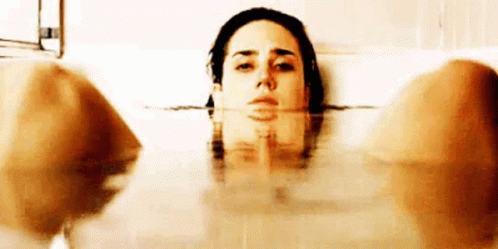 a woman is laying in a bathtub with her head above the water looking at the camera .