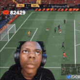 a man wearing headphones looks up at a soccer game with the number 82429 on the screen