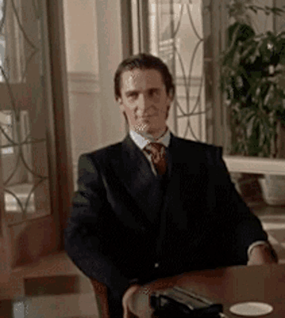 a man in a suit and tie is sitting at a table looking at the camera