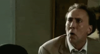 a man in a suit and tie is making a funny face while sitting at a table .