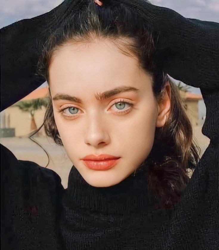 This may contain: a young woman with blue eyes wearing a black turtle neck sweater and holding her hair in the air
