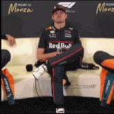 a man in a red bull shirt sits on a couch with his legs crossed