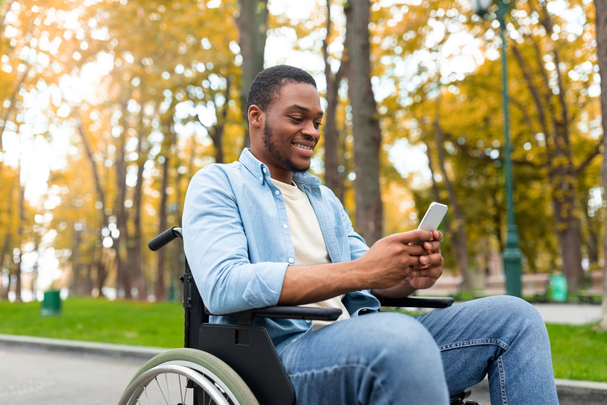 cheery-disabled-black-guy-in-wheelchair-using-mobile-phone-checking-email-or-messages-at-autumn.jpg