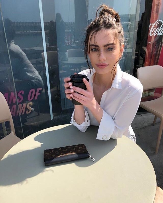 This may contain: a woman sitting at a table with a cell phone in her hand and looking at the camera