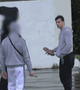 a man in a grey sweatshirt holds a skateboard in his hand