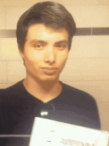 a man in a black shirt is holding a piece of paper in front of his face