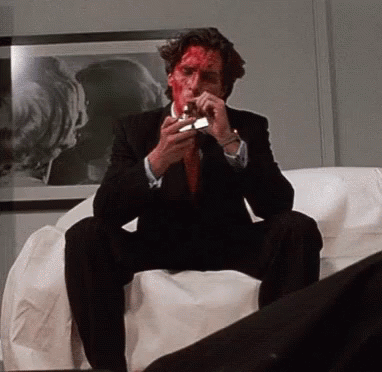 a man in a suit and tie is sitting on a couch lighting a cigarette with blood on his face .
