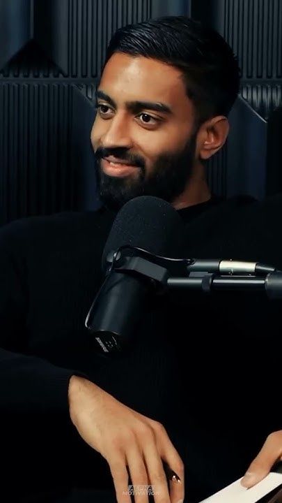 This may contain: a man sitting in front of a microphone holding a piece of paper and looking at the camera