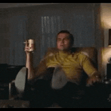 a man is sitting in a chair holding a bottle of beer and a cup of coffee .