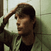 a man leaning against a wall holds his hand to his head