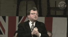 a man in a suit and tie stands in front of a british flag .