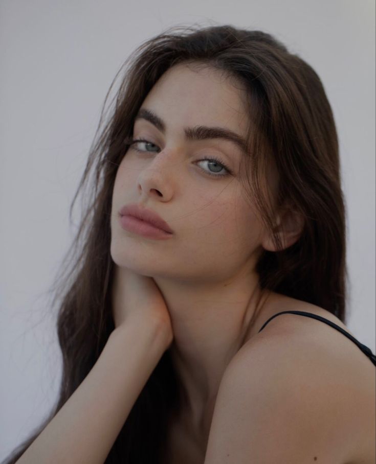 This may contain: a woman with long brown hair and blue eyes is posing for the camera while wearing a black tank top