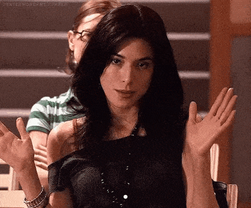 a woman with long black hair is sitting at a table with her hands up .
