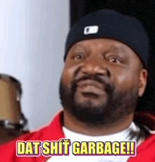 a man with a beard wearing a hat and a red jacket says dat shit garbage