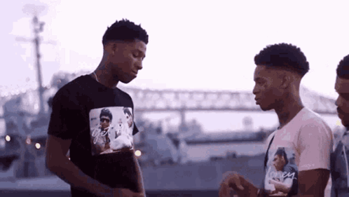 a group of young men are standing next to each other in front of a bridge and talking .