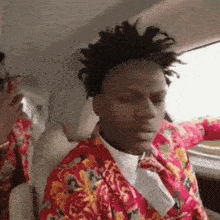 a man wearing a floral shirt and tie is sitting in a car