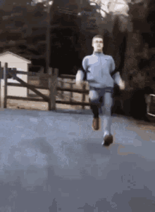 a man is running on a road with a fence in the background .