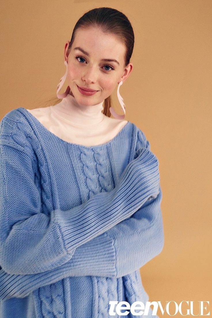 This may contain: a woman in a blue sweater poses for the camera with her hands on her hips