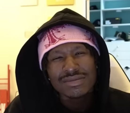 This may contain: a man wearing a pink and black hoodie is sitting in front of a book shelf