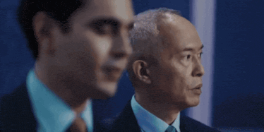 a man in a suit and tie is looking at another man