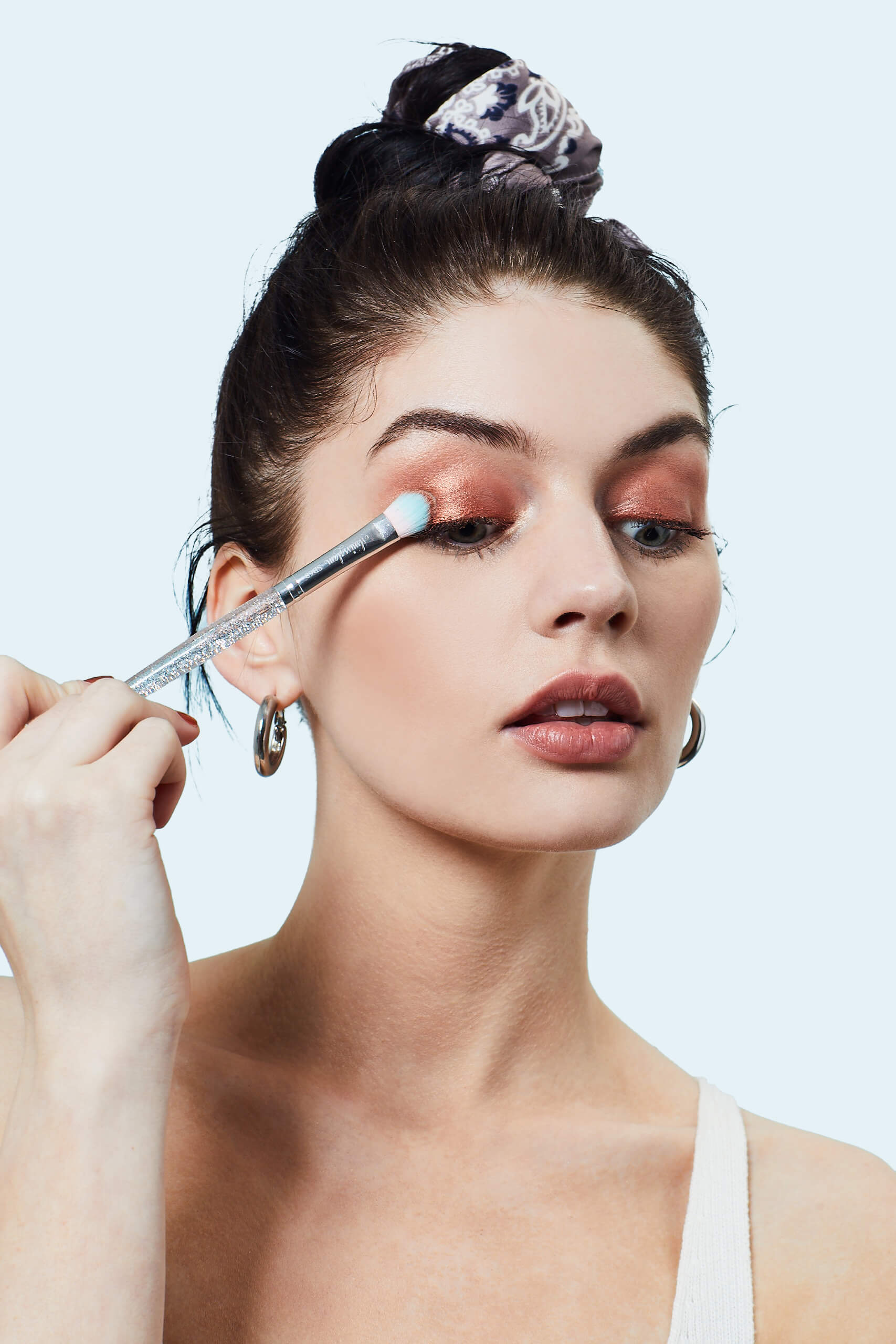 A photo of a woman applying a shimmery bronze eyeshadow using a small brush