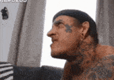 a man with tattoos on his face is sitting on a couch . a man with tattoos on his face is sitting on a couch .