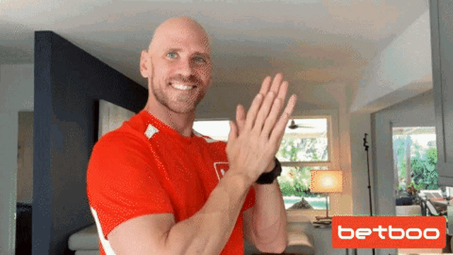 a bald man in a red shirt is clapping his hands in front of a betboo logo a bald man in a red shirt is clapping his hands in front of a betboo logo