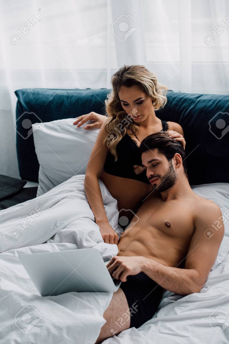 141921204-muscular-man-looking-at-laptop-near-attractive-woman-on-bed.jpg